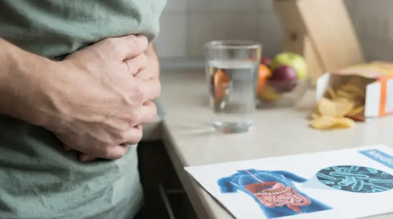 Persona con le mani sull'addome accanto a un bicchiere d'acqua e un'immagine del tratto digerente