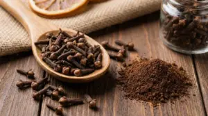Chiodi di garofano interi e macinati su un tavolo di legno con cucchiaio di legno