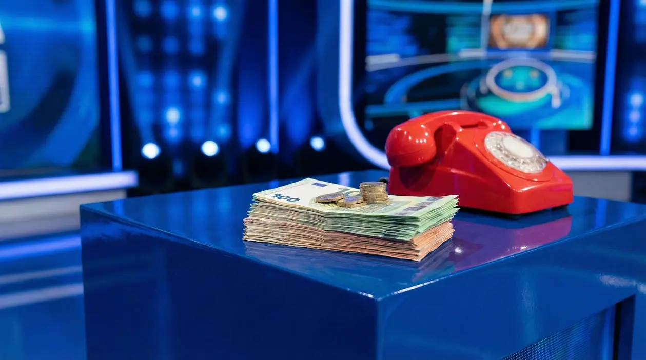 Mazze di banconote e monete su un tavolo accanto a un telefono rosso nello studio di un game show